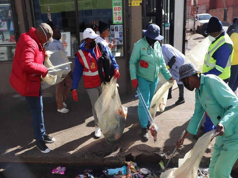 Volunteers and city officials participating in a large-scale clean-up of Hillbrow's streets as part of the Mandela Day campaign, showcasing community effort and transformation.